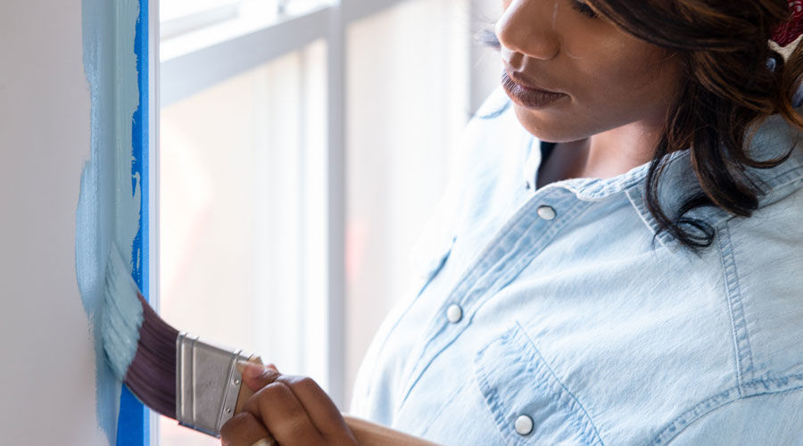 Woman painting wall next to window with brush