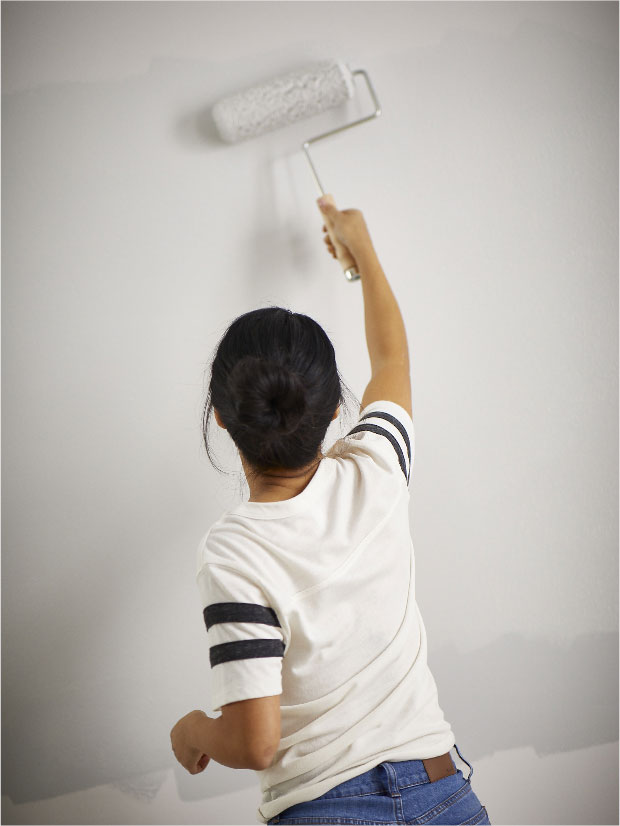 Woman painting a wall to white with pain roll.