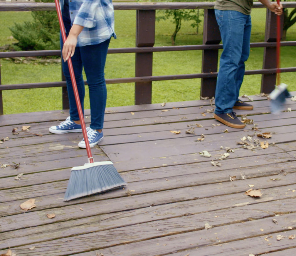 man and woman are cleaning deck with broom