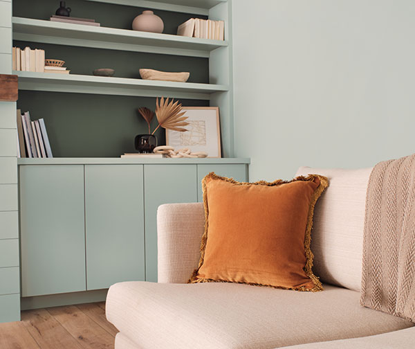 Close up of beige couch with burn orange pillow. Walls in background painted Copen Blue SW 0068