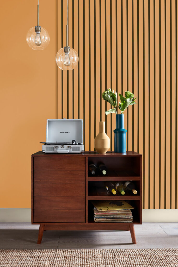 Vignette of a half-paneled wall that's golden yellow. Also features a vintage cabinet housing a bottle of wine and a record player. 