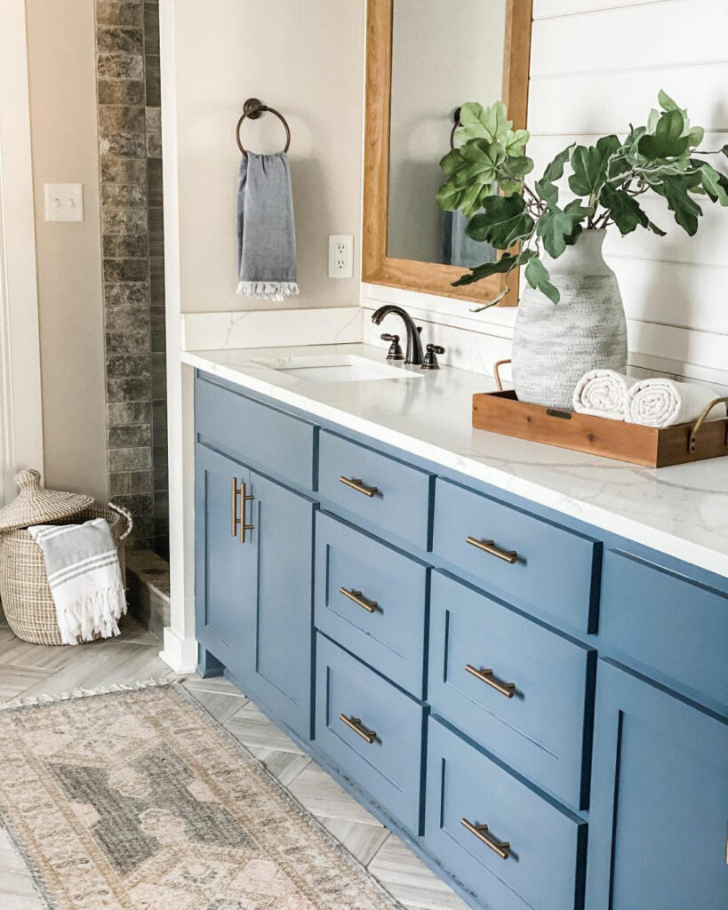 Bathroom vanity with blue cabinets, shiplap walls and natural decorations like wood frame mirrors..