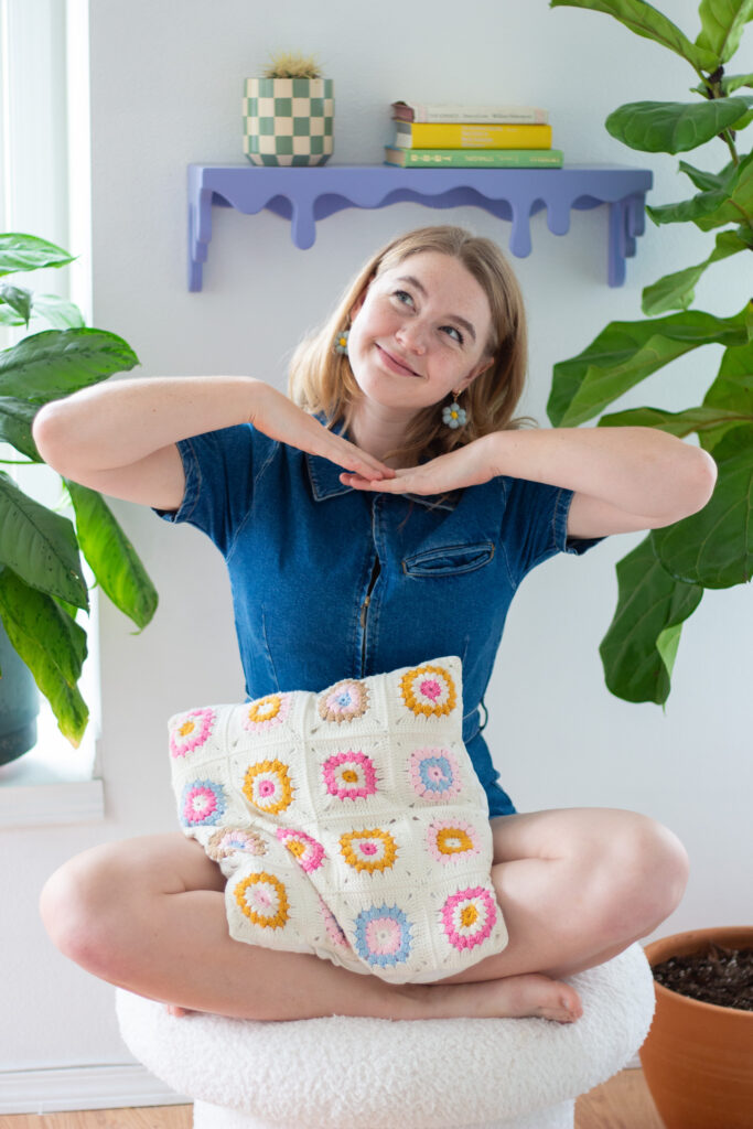 Annika Hinds of Blondesigns perched smiling on a boucle stool with pillow in lap.