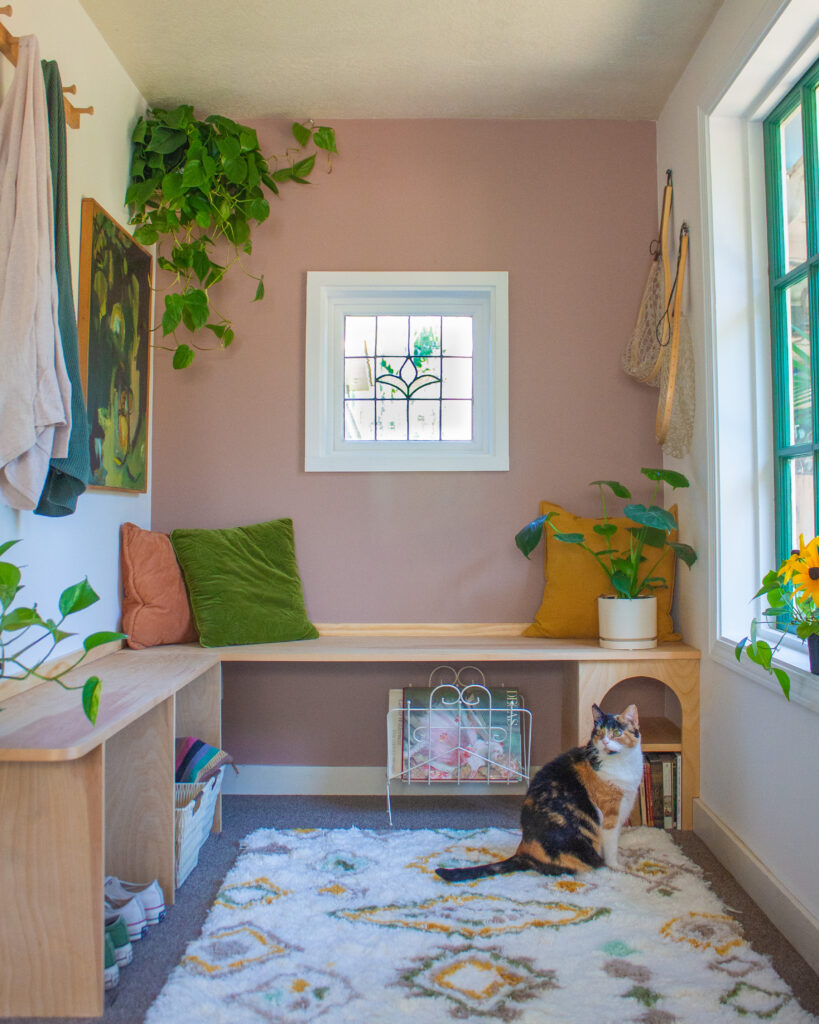 An entryway space painted in 2023 Color of the Year Redend Point SW 9081 with a stain-glass window above a wooden bench. A cat
