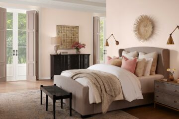 Bedroom image with cozy bed layered with throws and pillows and tall exterior doors in the background bringing in natural light.