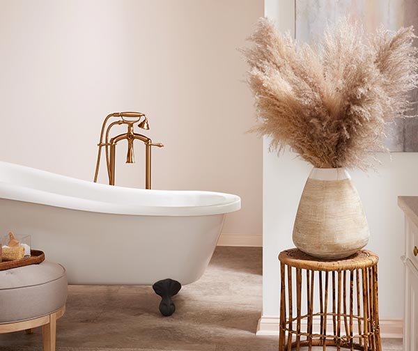 Vignette of a bathroom with a claw foot tub and an earthen container filled with wispy wheat-colored plumes of pampas grass.