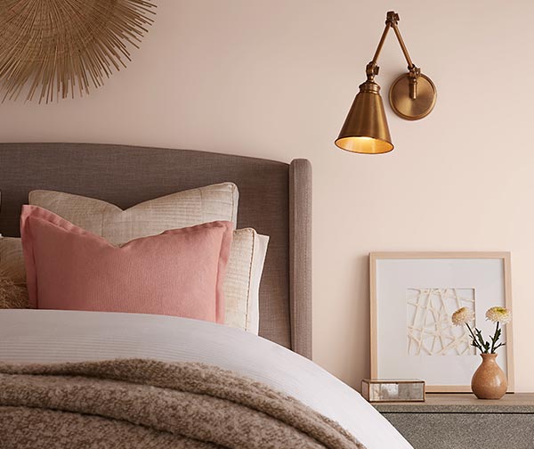 Cropped image of a cozy bed with layers of throws and pillows and a bedside table with a small vase and cut flowers.