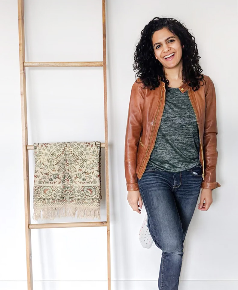 Feature image of blogger Hana Sethi leaning against a white wall dressed casually in blue jeans and a caramel-colored leather jacket.
