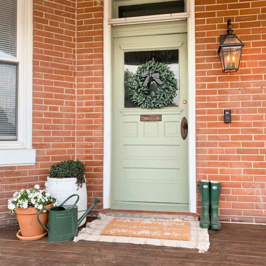 Front door painted in Clary Sage with a boxwood wreath and boots to the right.