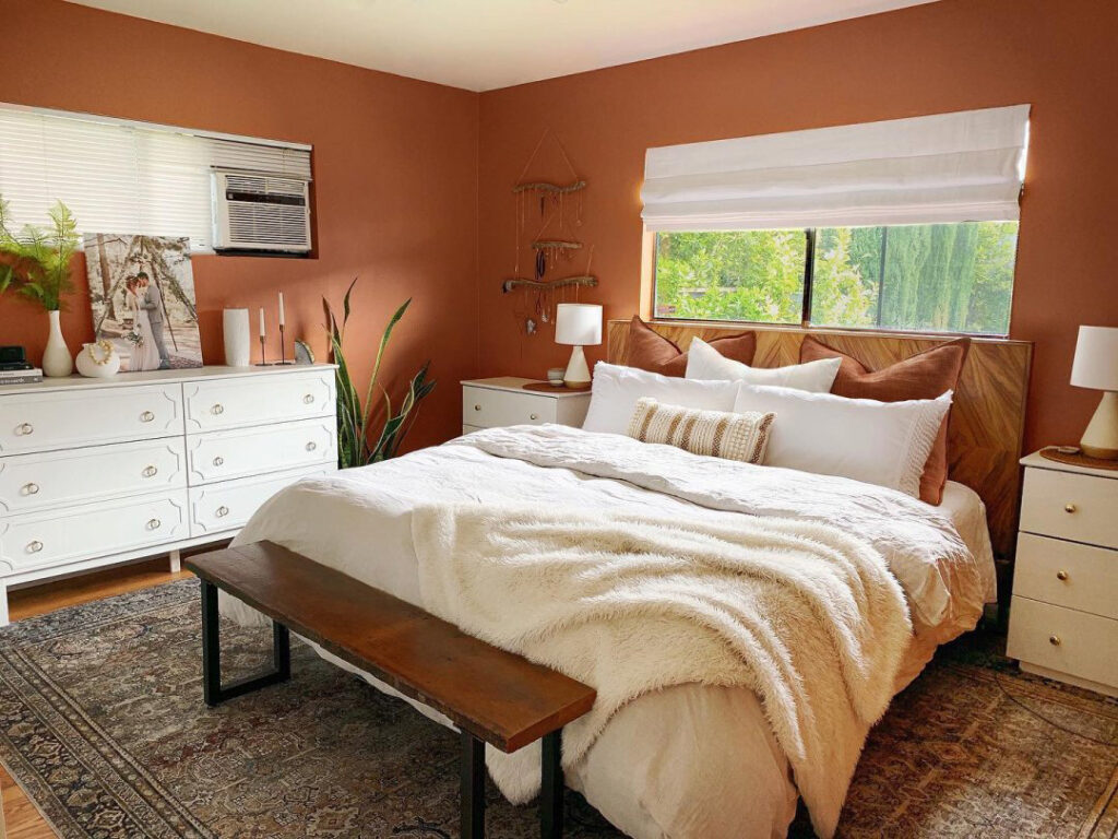 Bedroom scene with cozy bed and layered linens. Walls painted in Cavern Clay SW 7701.