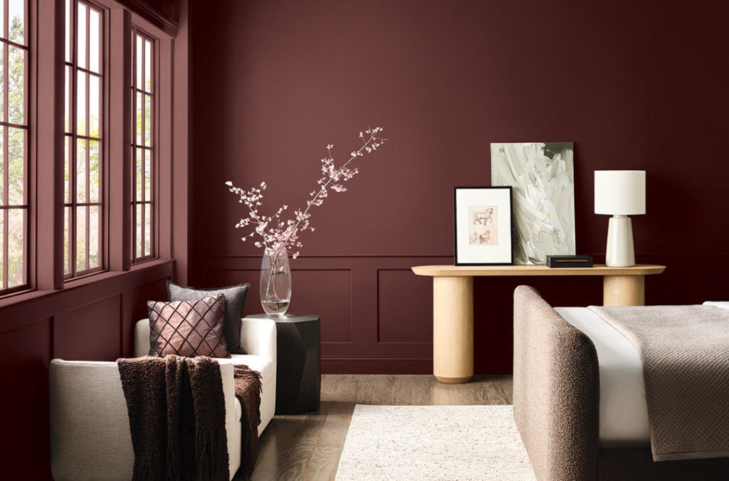 A modern bedroom space with two sitting chairs and the foot of a bed with walls painted in Rojo Marron.