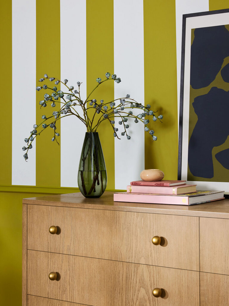 Close cropped image of a dresser with striped wall painted with Offbeat Green SW 6706.