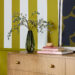 Close cropped image of a dresser with striped wall painted with Offbeat Green SW 6706.